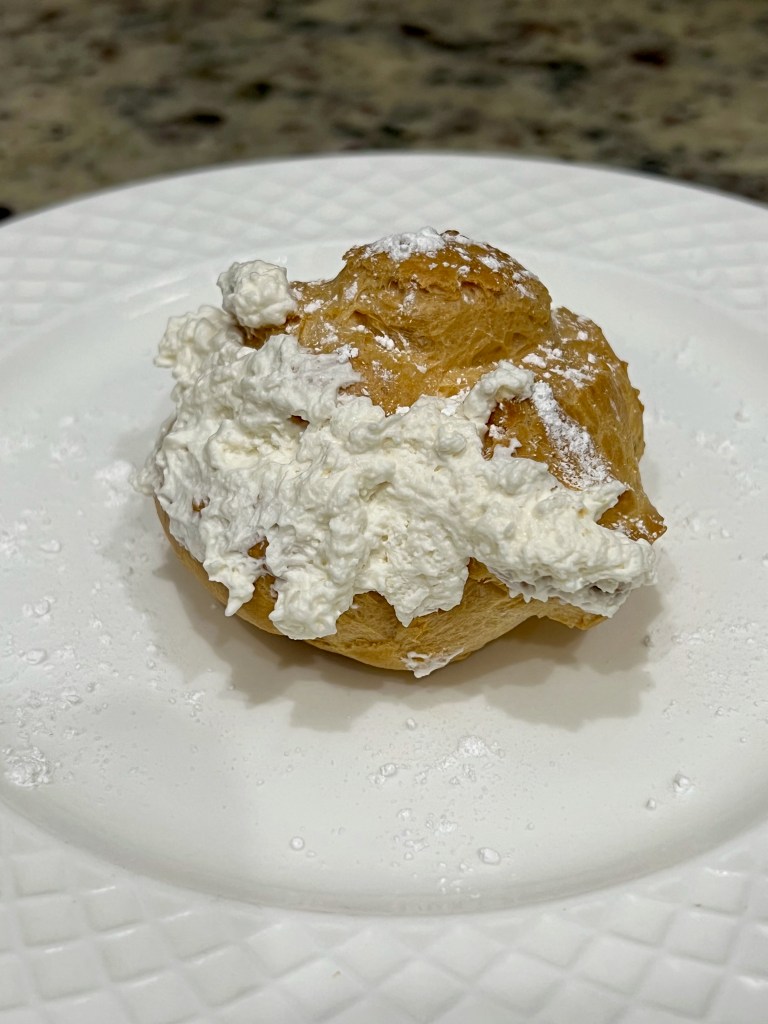 A cream puff dusted with sugar sits on a plate. 