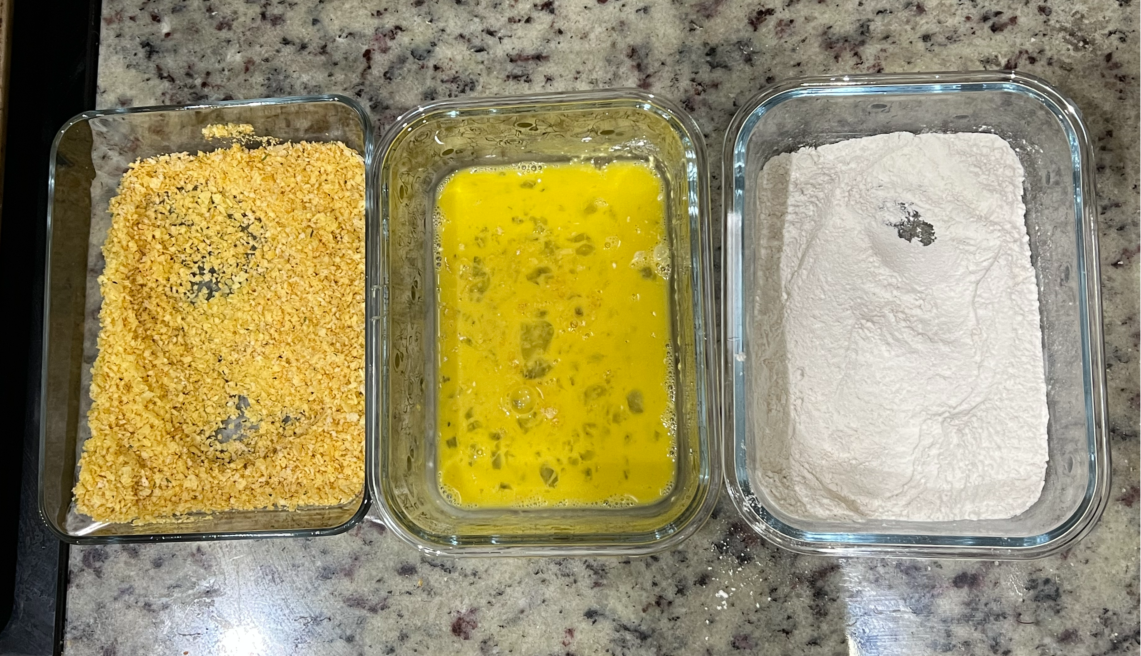 A breading array. A container of flour, a container of eggs, and a container of pulverized chips and bread crumbs.